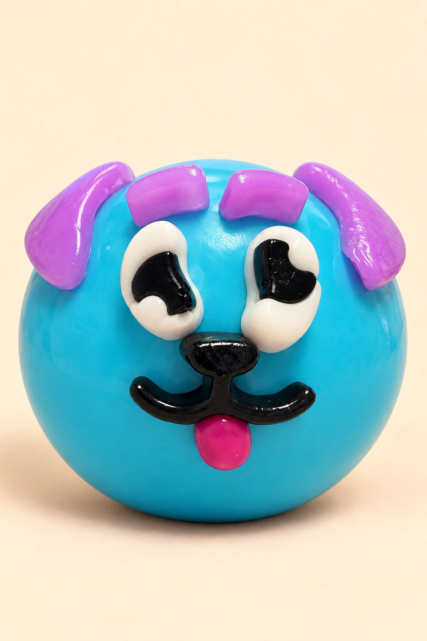 Blue crunchy face-swap squishy ball with lavender face pieces, white eyes, black nose and smile, and pink tongue; shown outside plastic pouch