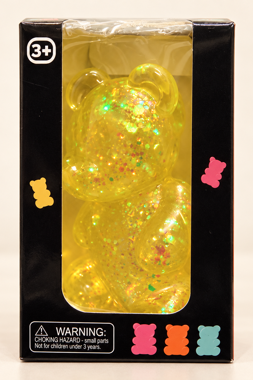 Yellow glitter gummy bear squishy in black window box, front studio detail; AI-assisted