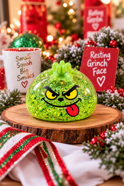 Individual green glitter Mini Grinch mystery dumpling pinch squishy with tongue-out face in a professional holiday scene