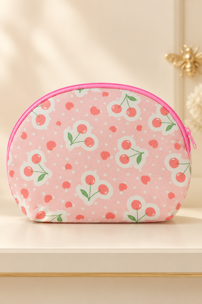 pale blush pink background, paired coral cherries in white scalloped medallions, coral hearts and small white dots; pink zipper and piping cherry-print makeup bag. One selected bag per purchase.