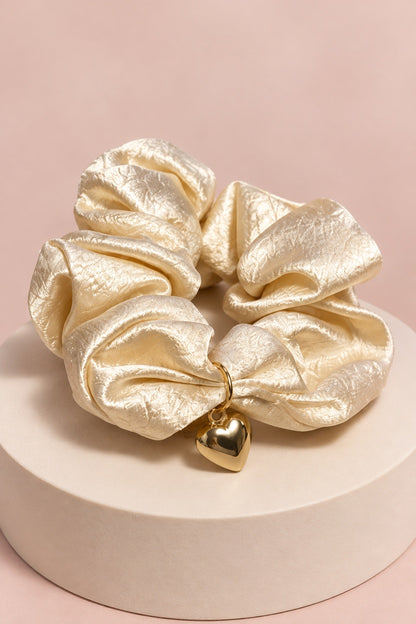 Champagne Melody heart-charm scrunchie with glossy gathered fabric and gold-tone heart