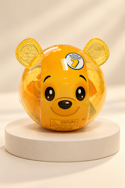 Sealed yellow glitter bear capsule, sharp front studio view on ivory pedestal